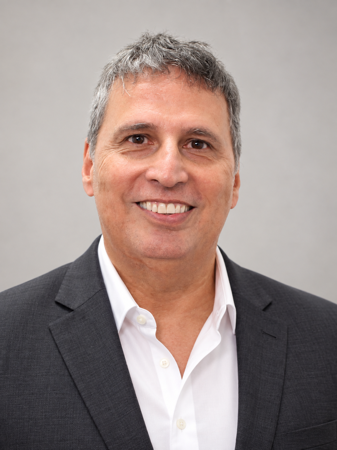 Juan Mejía smiling, wearing a charcoal jacket and white open-collar shirt